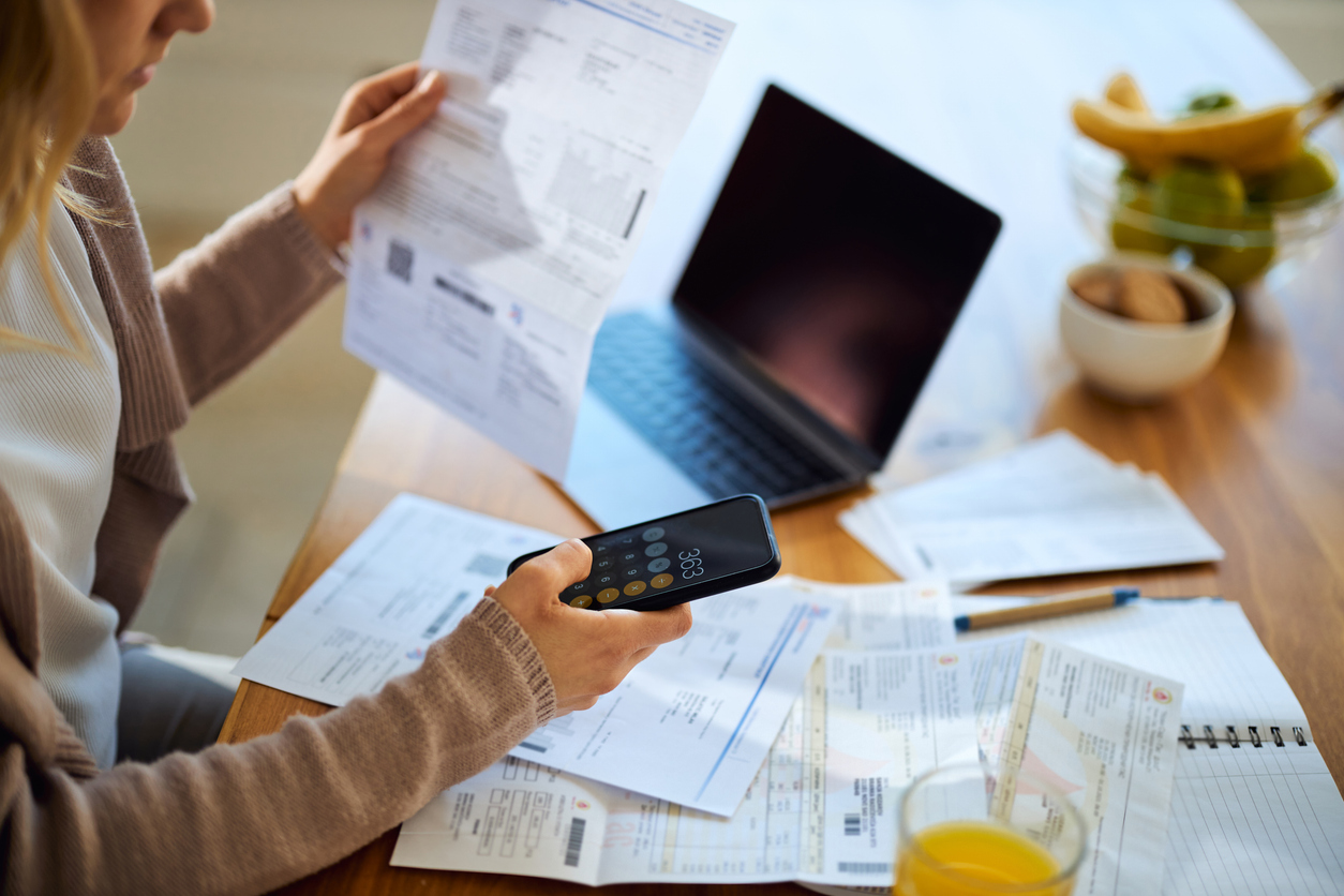 a woman using a calculator to add up her bills whilst looking and paying for her bills